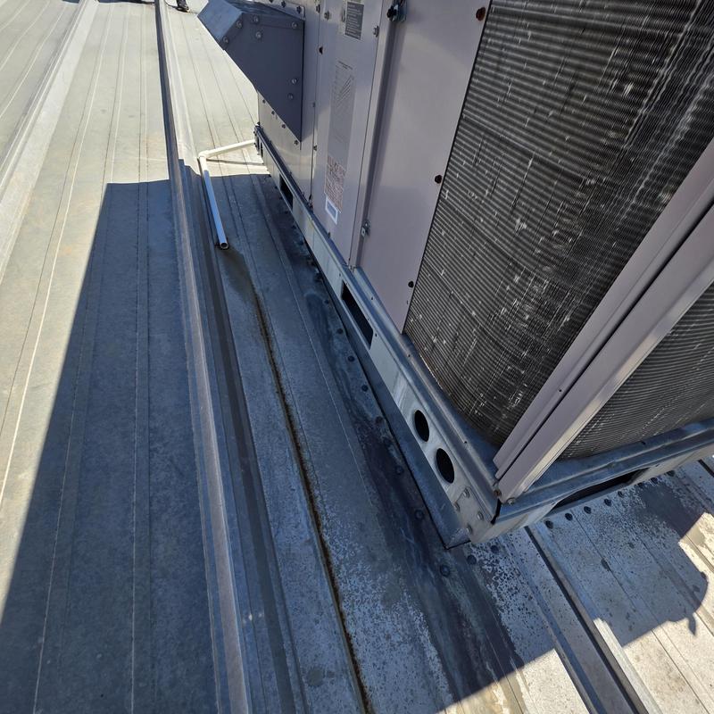 HVAC unit base on metal roof with water stains