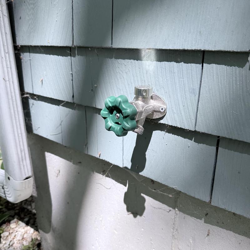 Outdoor hose bib with green valve handle on siding