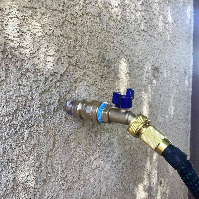 Hose bib with attached garden hose on stucco wall
