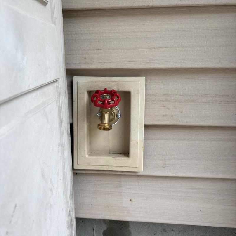 Outside faucet with red valve handle installed on siding