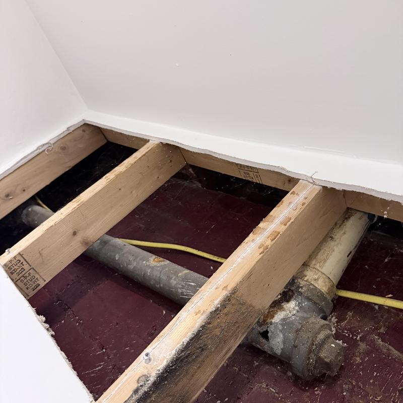 Shower drain pipe exposed with wood joists above