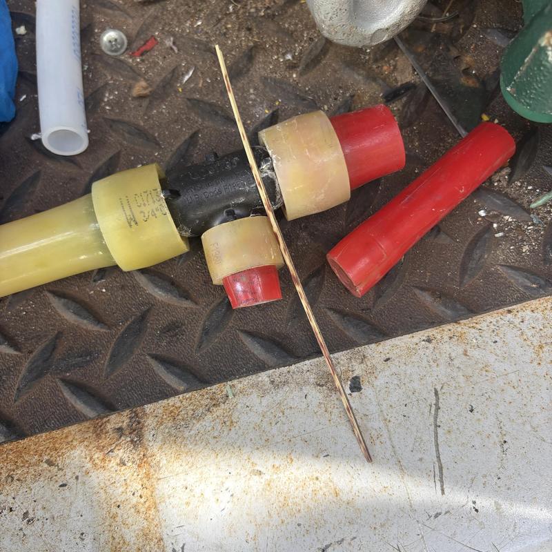 PEX tee fitting with damaged red pipe sections on metal floor