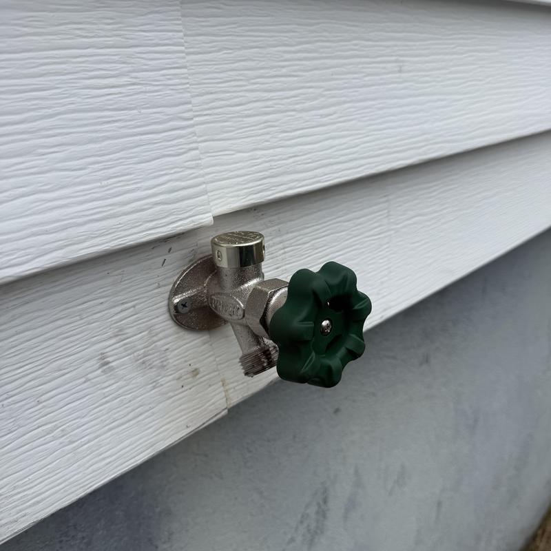 Outside faucet with green handle on white siding