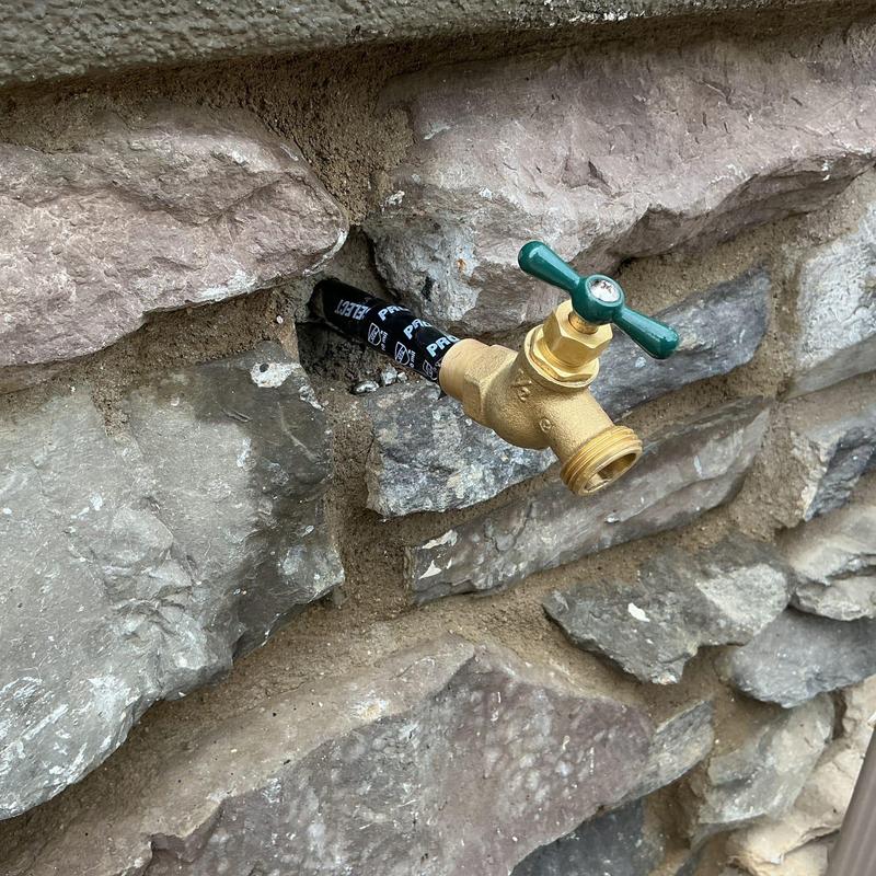 Copper hose bib installation on stone wall exterior