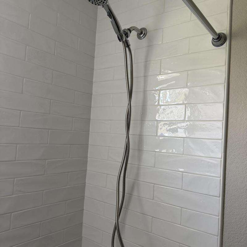 Shower head with flexible hose on white tile wall Shower head with flexible hose on white tile wall