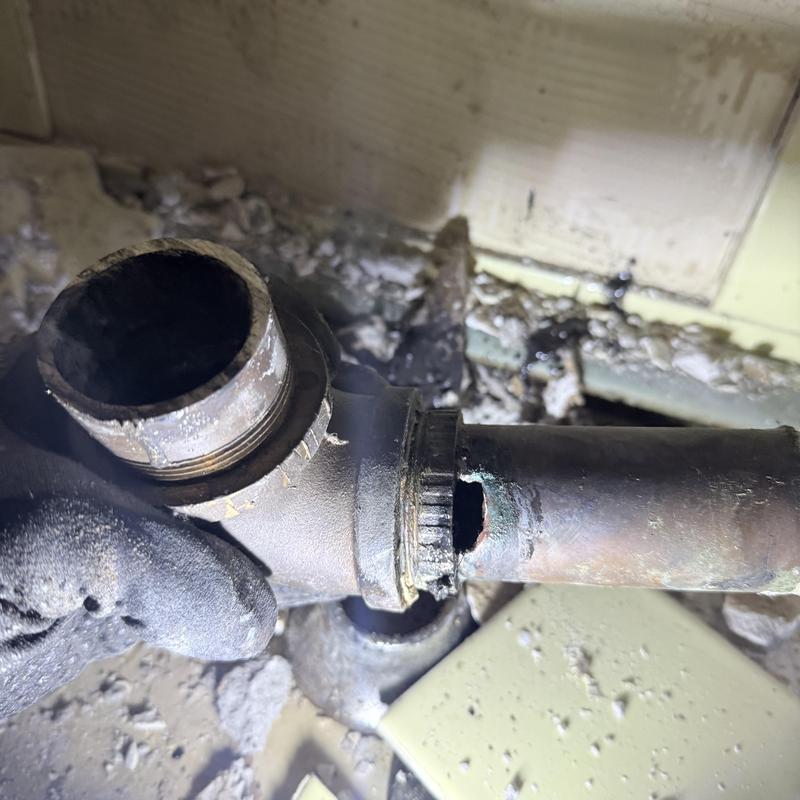 Bathroom drain pipe with large corrosion hole visible