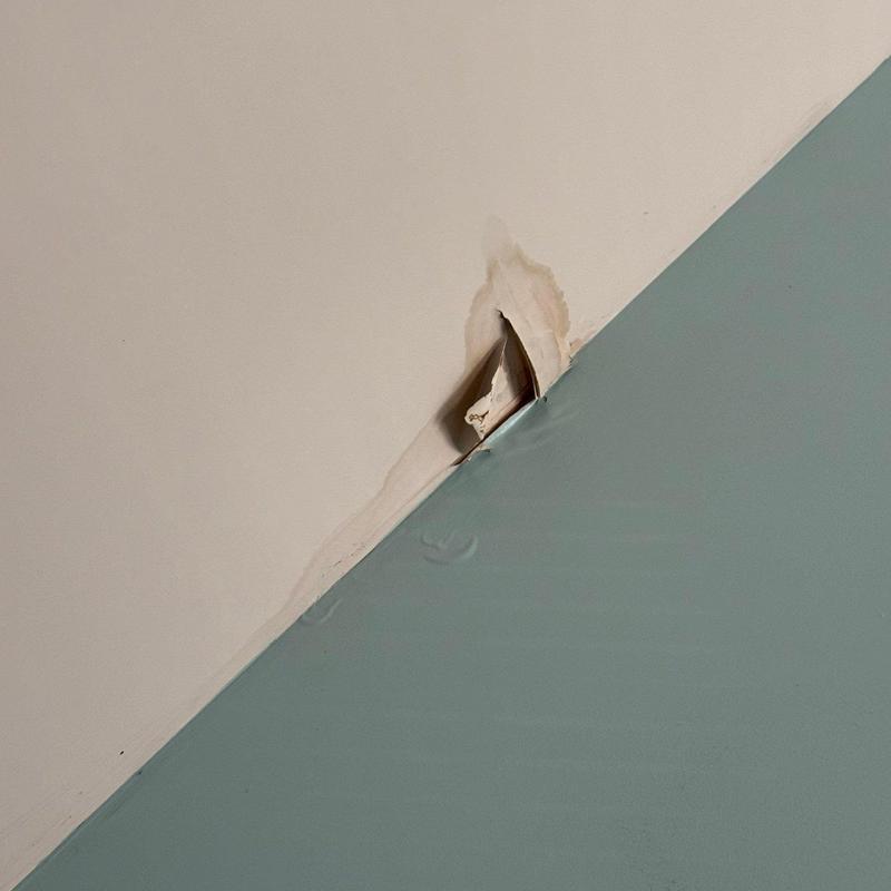 Drywall corner damage with peeling paint and stains