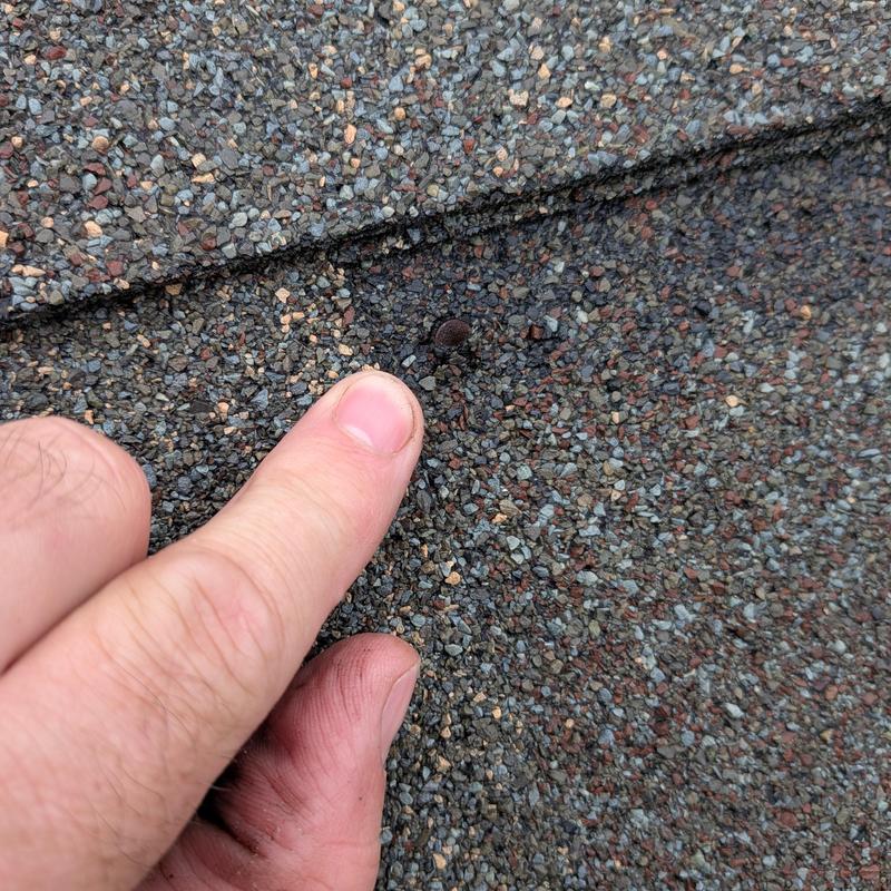Roofing shingle with nailed patch close-up and finger point Roofing shingle with nailed patch close-up and finger point