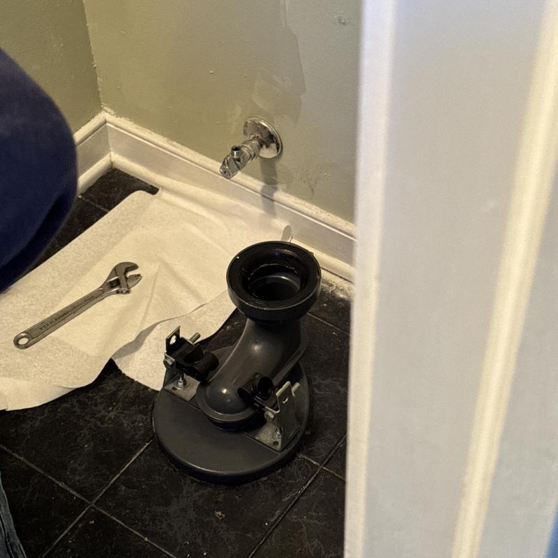 Toilet flange with wrench beside shut off valve on black tile Toilet flange with wrench beside shut off valve on black tile