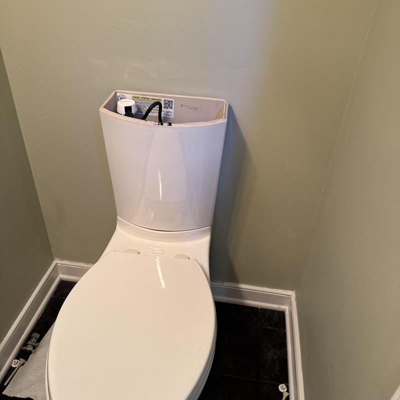 One-piece toilet with exposed tank components in bathroom corner One-piece toilet with exposed tank components in bathroom corner