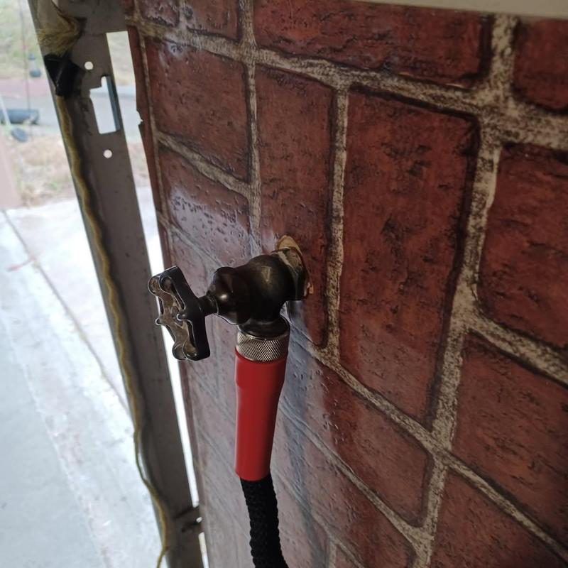 Outdoor hose bib with attached garden hose on brick wall