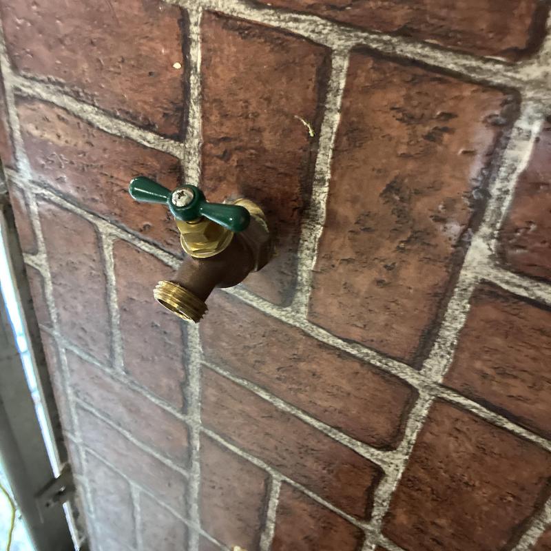 Outdoor hose bib with green handle on brick wall