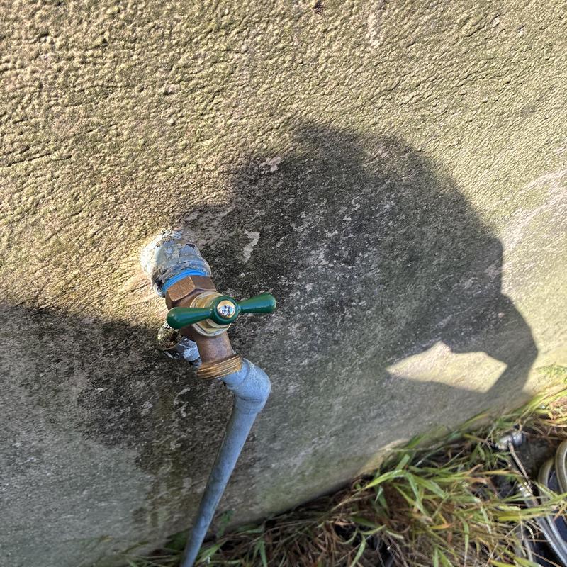 Outdoor hose bib with green handle on concrete wall