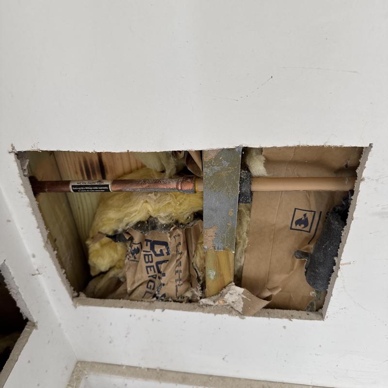Copper plumbing pipe behind drywall with insulation visible Copper plumbing pipe behind drywall with insulation visible