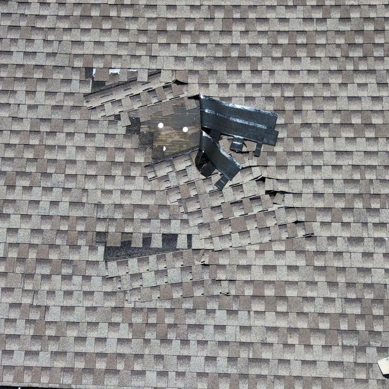 Roof shingles damaged by high winds revealing wood deck Roof shingles damaged by high winds revealing wood deck
