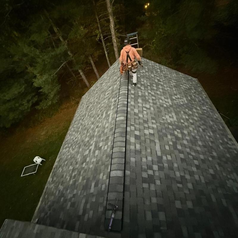 Asphalt shingle roof installation with worker on ridge Asphalt shingle roof installation with worker on ridge
