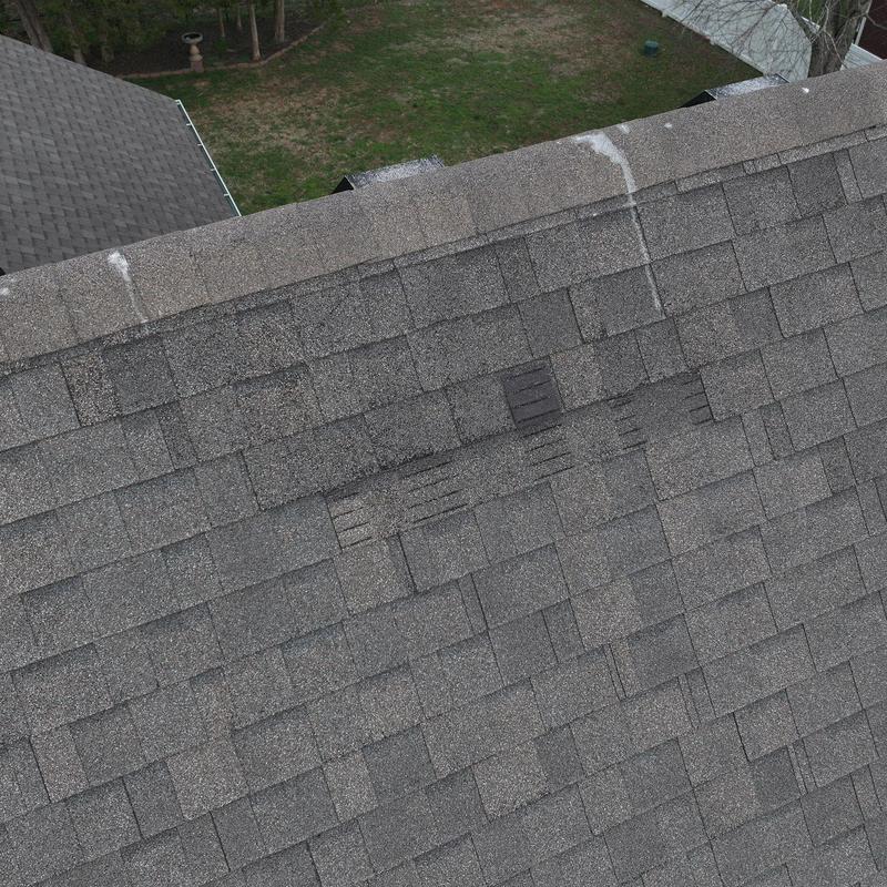 Asphalt shingles with visible hail damage on roof ridge
