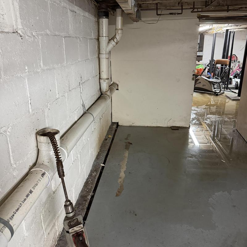 PVC drainpipe with plumbing snake in wet basement floor PVC drainpipe with plumbing snake in wet basement floor