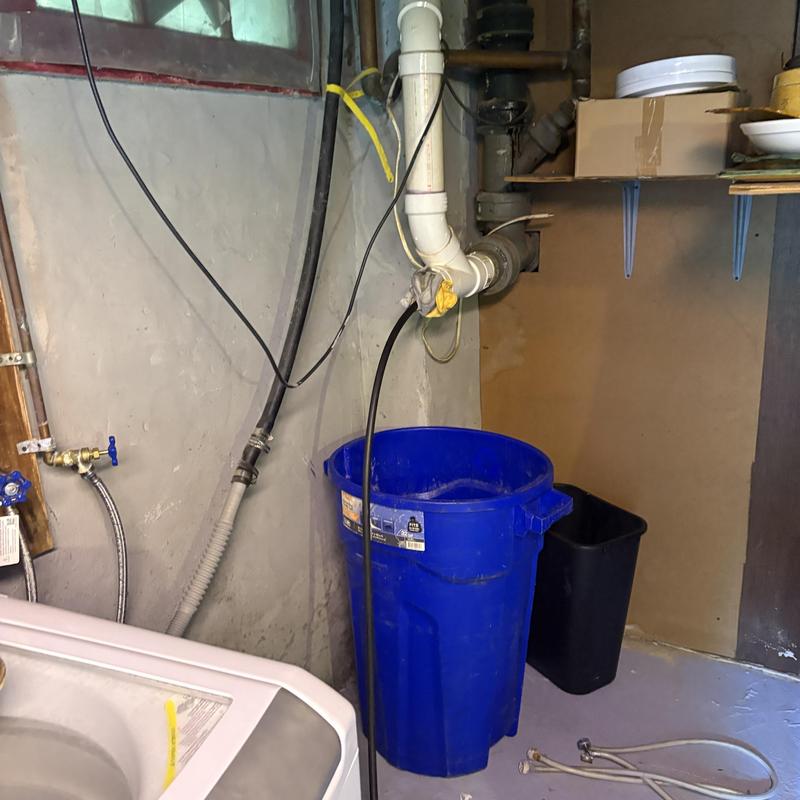 Drain pipe jetting with blue catch bucket in laundry room Drain pipe jetting with blue catch bucket in laundry room