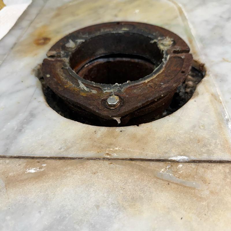 Toilet flange with rusted mounting bolts on tile floor