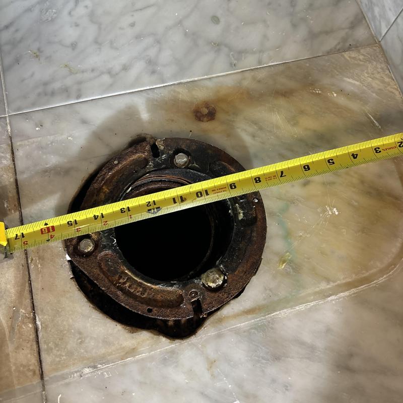 Toilet flange with measuring tape on tiled floor
