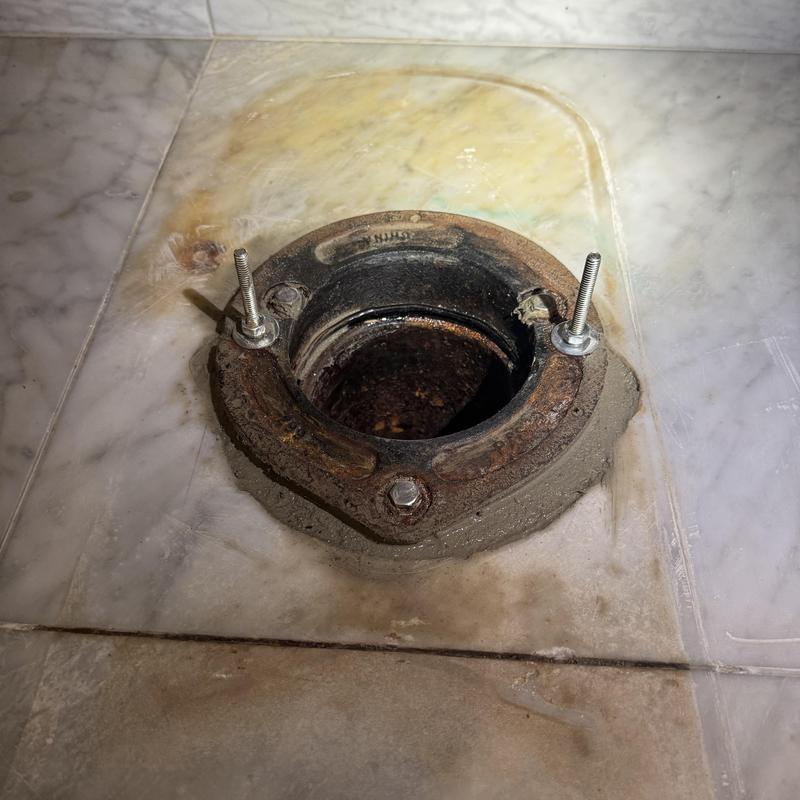 Toilet flange secured with fresh concrete on tile floor