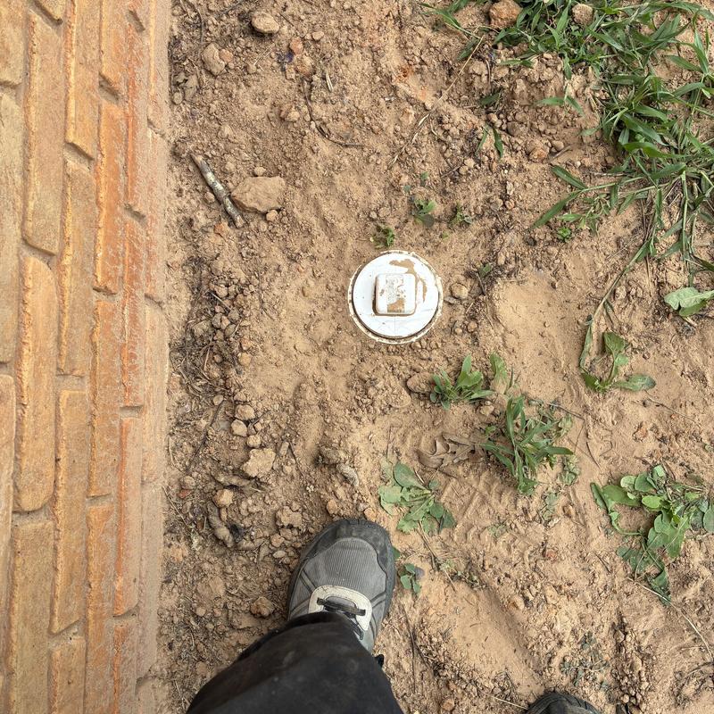 Sewer cleanout cap in dirt near building wall