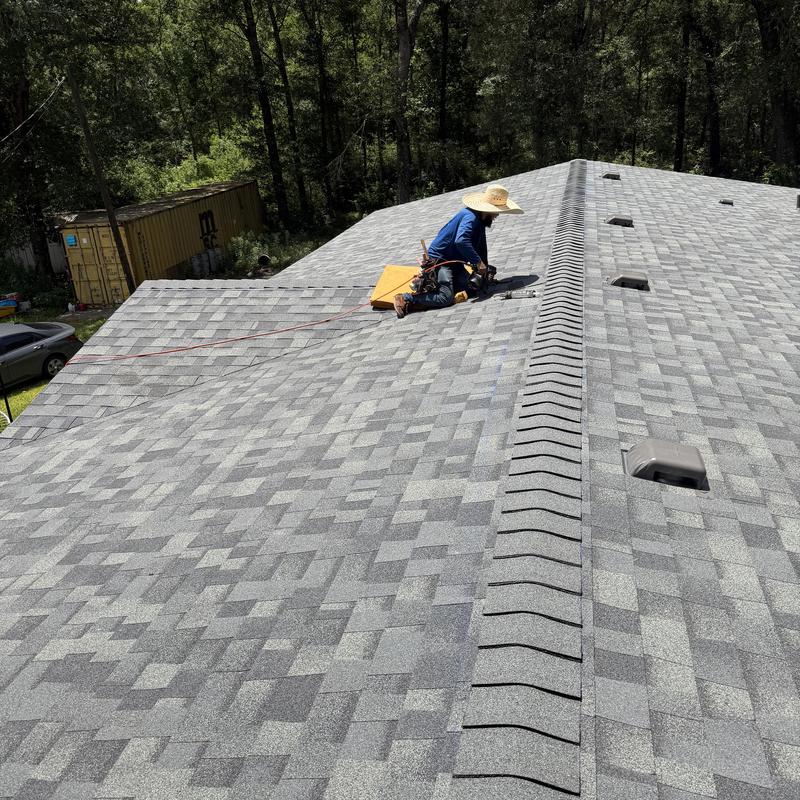 Asphalt shingle roof with worker installing ridge vent
