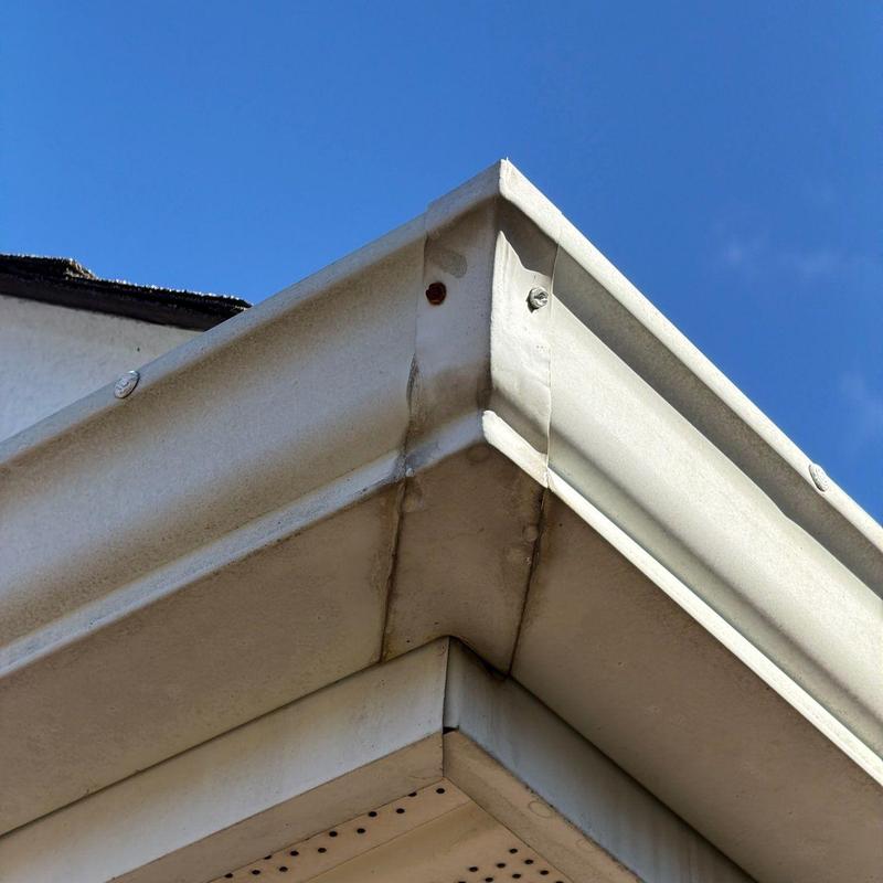 Metal gutter corner joint with visible rust and stain