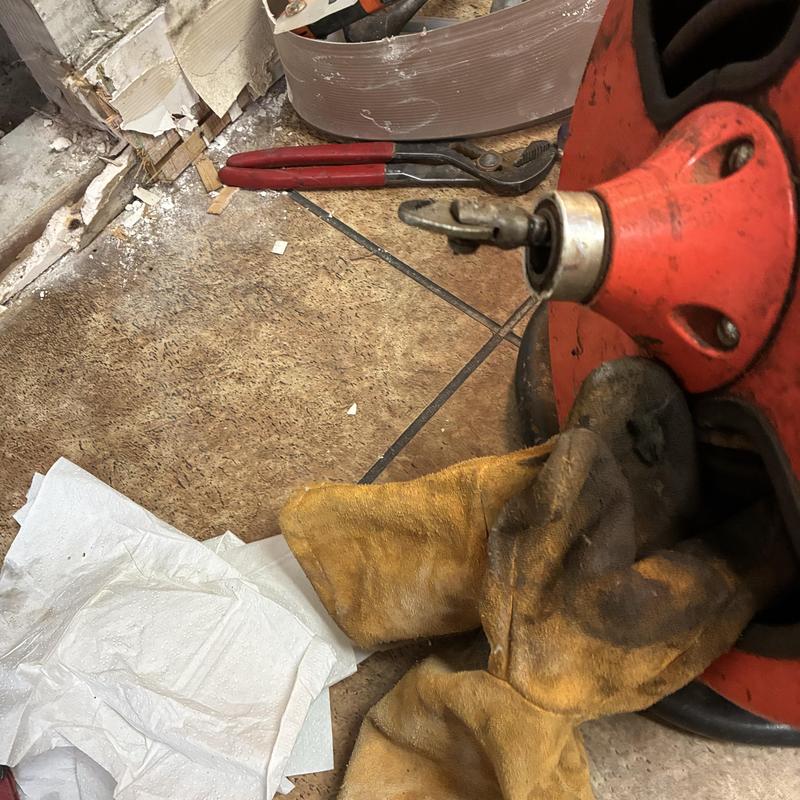 Drain cleaning machine and work gloves on tile floor