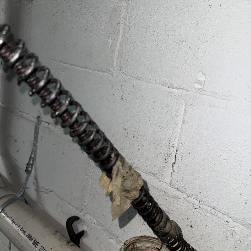 Drain cleaning auger cable with wrapped debris on basement wall Drain cleaning auger cable with wrapped debris on basement wall