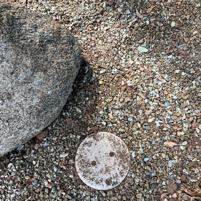 Water main valve box next to large rock in gravel