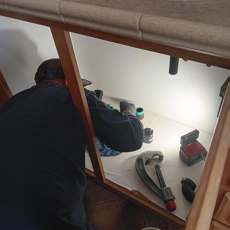 Drain line plumbing under kitchen sink with tools and technician