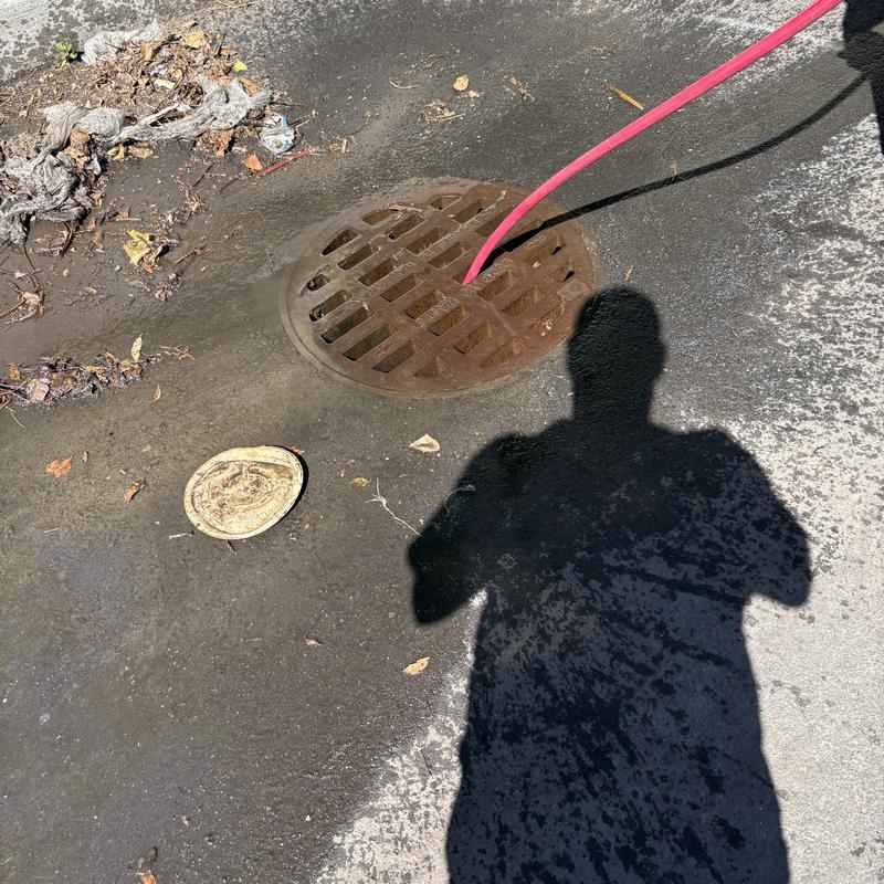 Storm drain cleaning with red jet hose in asphalt driveway Storm drain cleaning with red jet hose in asphalt driveway