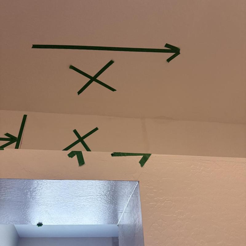 Drywall ceiling marked with green tape arrows and Xs