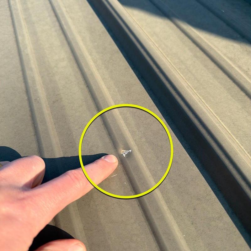 Metal roof panel damage with finger pointing at chip