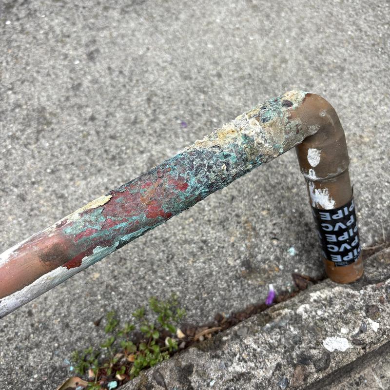 Corroded exterior copper water line section outdoors