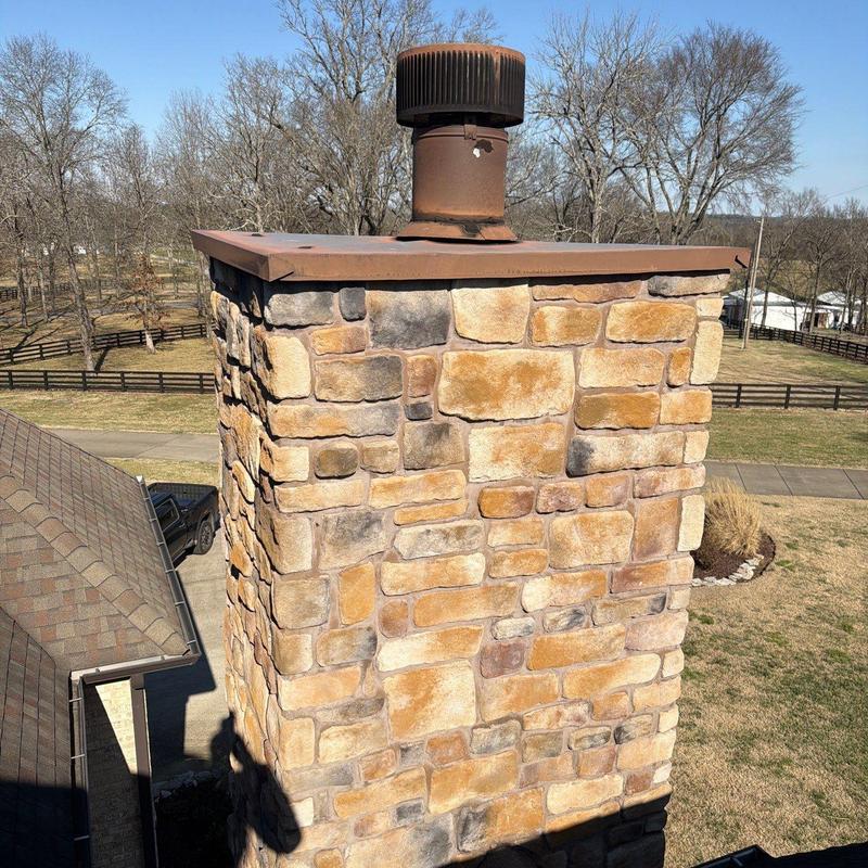 Stone chimney with metal vent cap on residential roof