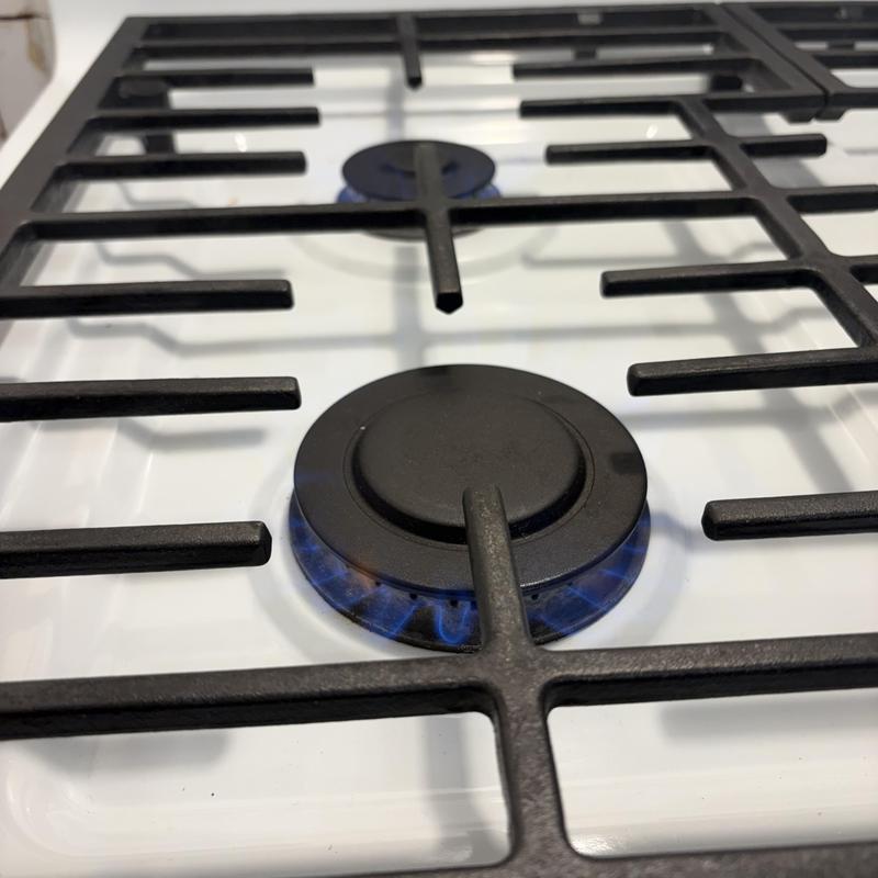 Gas stove burner with lit blue flame on white stovetop