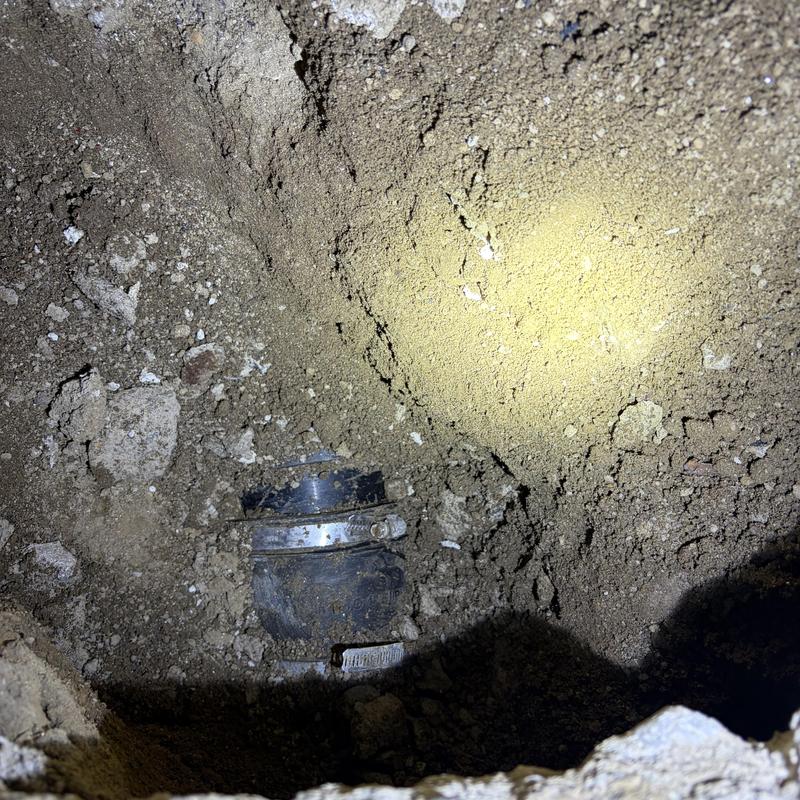 Basement plumbing pipe with clamp amid soil excavation