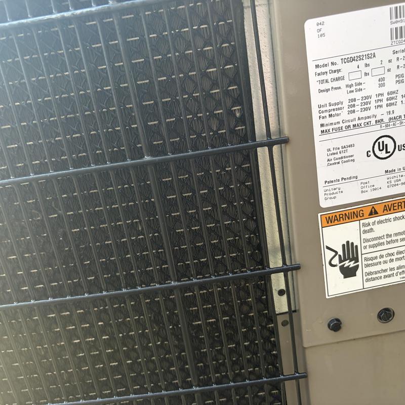 Outdoor AC condenser coil with debris buildup and label