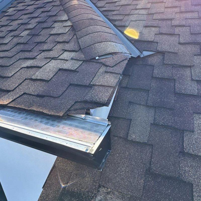 Roof shingles lifted near metal flashing on roof slope