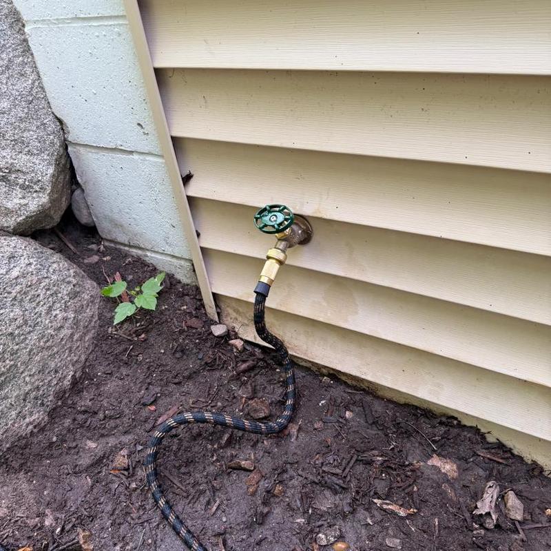Outdoor water spigot with attached garden hose near house wall