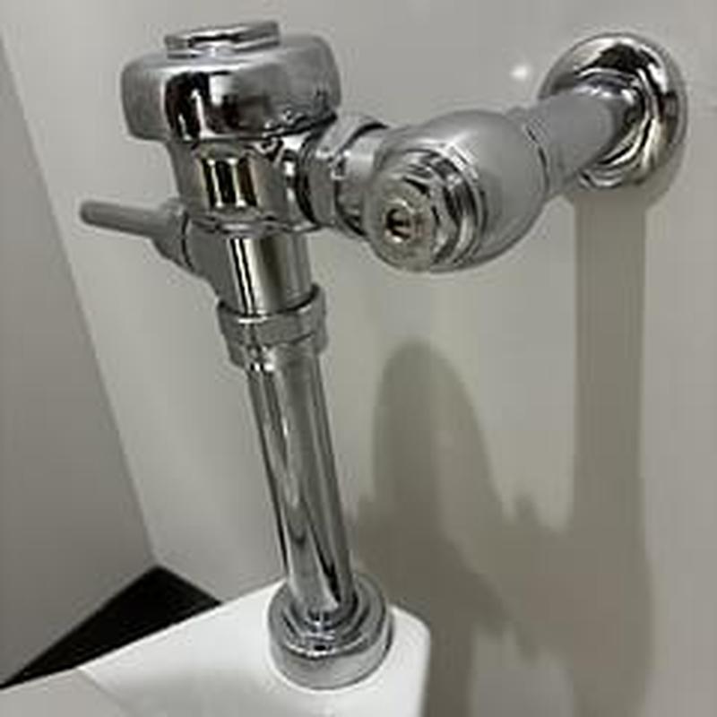 Flushometer valve and pipes in restroom corner