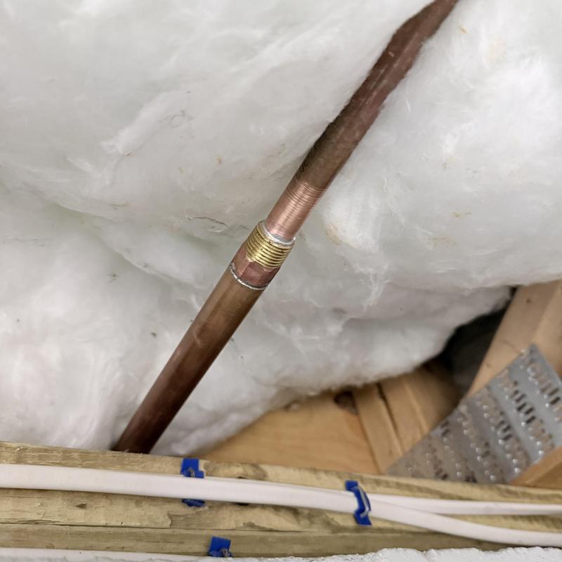 Copper plumbing pipe with brass fitting in attic insulation Copper plumbing pipe with brass fitting in attic insulation