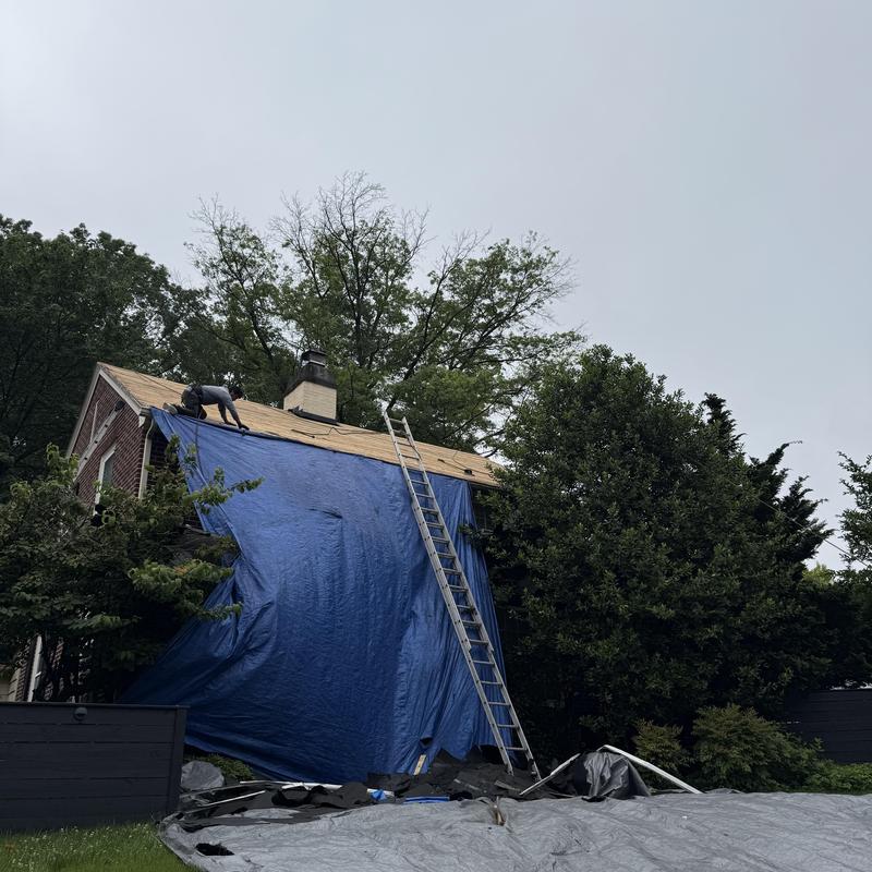 Wind-damaged roof with temporary tarp cover and ladder