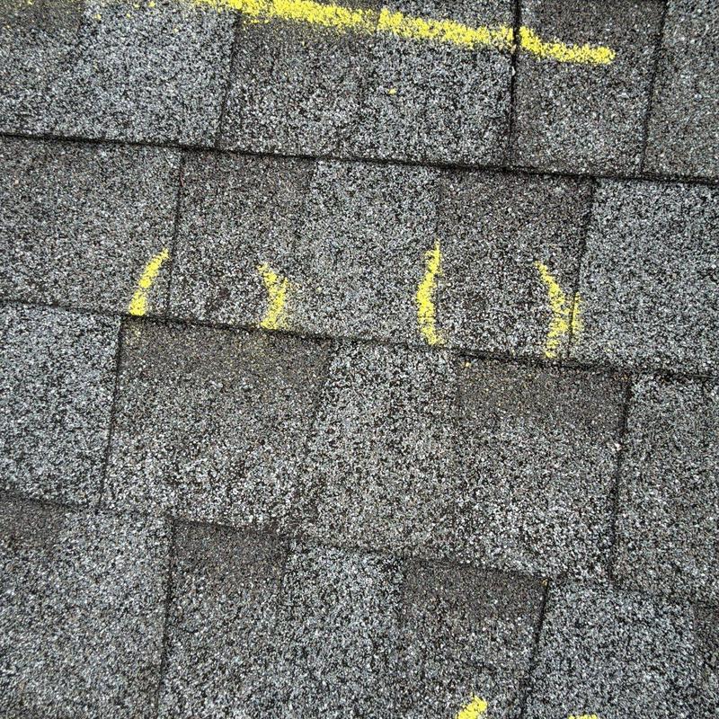 Asphalt roof shingles with hail damage marked for repair