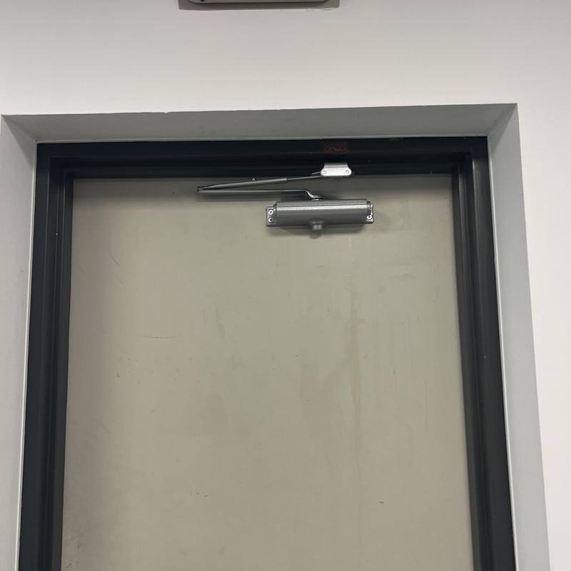 Door closer on beige metal door with black frame