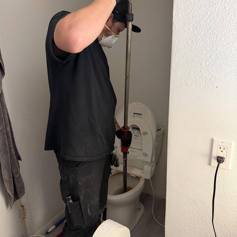Toilet auger clearing clog with plumber in bathroom Toilet auger clearing clog with plumber in bathroom