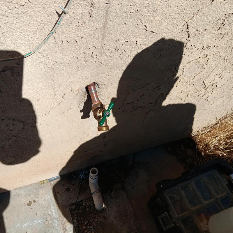 Hose bib with green handle mounted on stucco wall